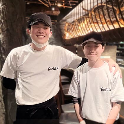串・肉・寿司 酒場ごはん すみかの男性アルバイト2人が笑顔で肩を組んでいる。